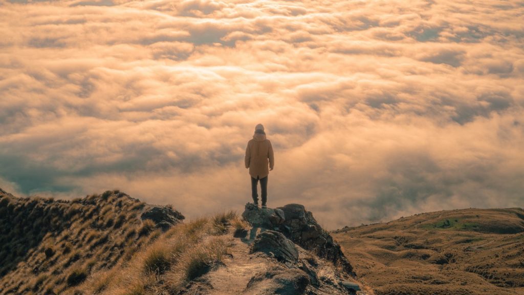 person on moutain overlooking clouds