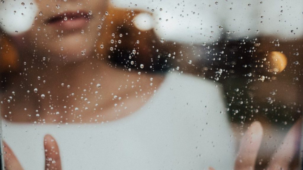 woman looking through window with rain on it