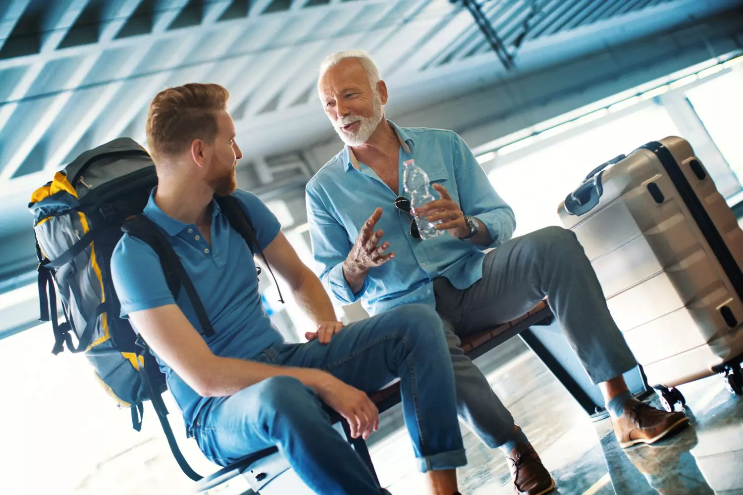 a young man and an old man talking to each other in an airport - Want to be happier? Talk to strangers.