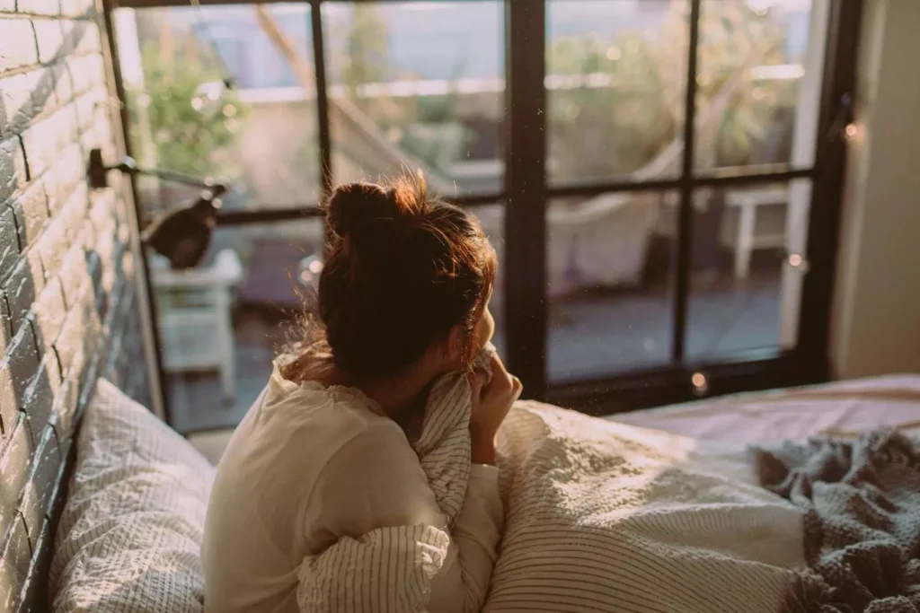 woman sitting up in her bed in the morning, looking out a window