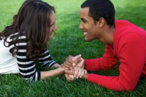 engaged couple lying in the grass holding hands and looking into each other's eyes