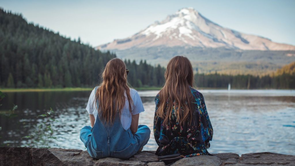 women sitting by mountain lake
