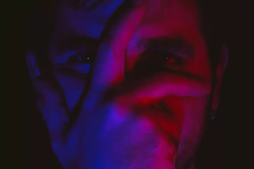 a man with his hand on his face, blue and red light shining on him. He's frustrated by politics
