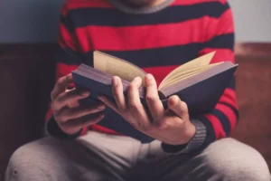 a man in a striped sweater holding an open book, praying