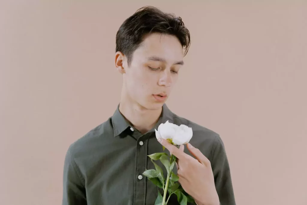 man holding and looking at a white flower