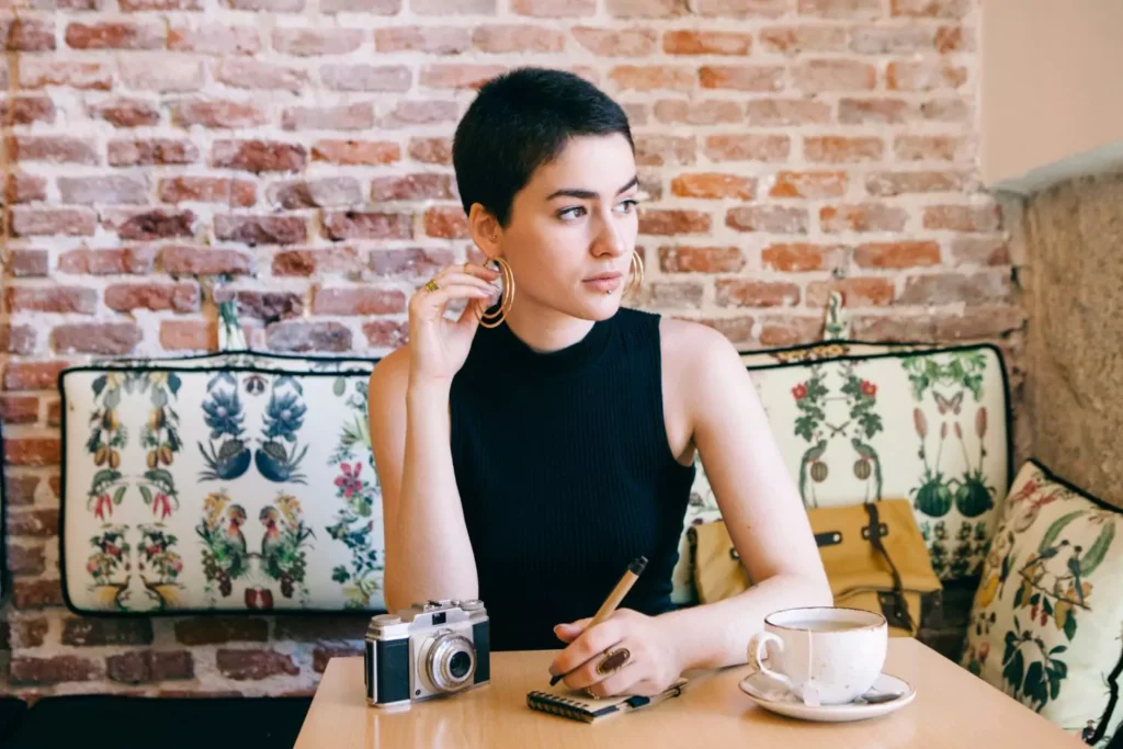 a single woman sitting in a coffee shop playing with her earring and looking out a window