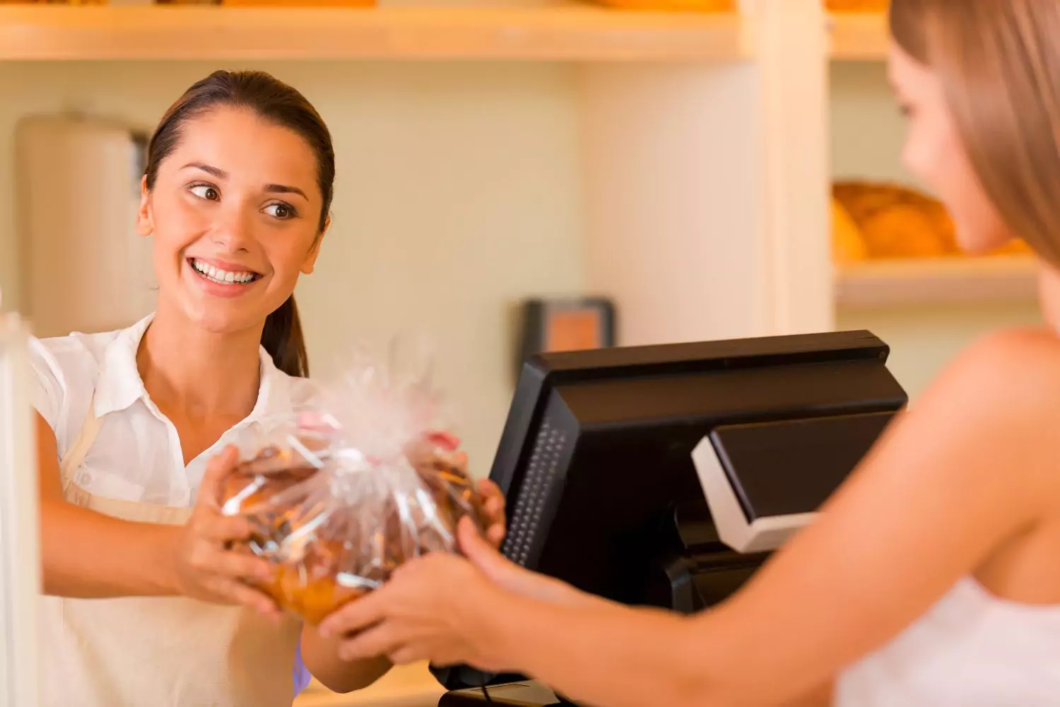 female worker handing a customer a bag of cookies over the counter, people pleaser