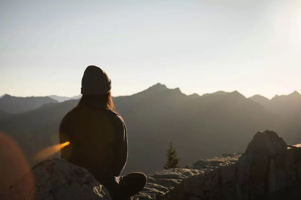 a woman sitting at the top of a mountain at dawn, no longer in despair