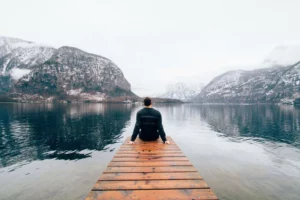 Guy sitting at the end of a dock looking out over a mountain lake