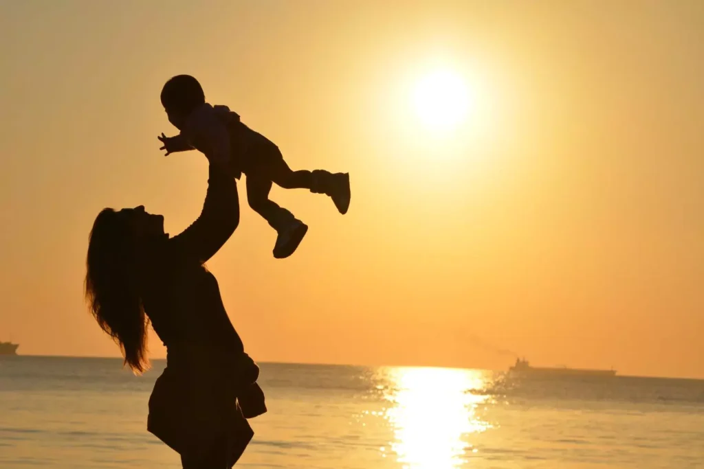 a woman holding her child in the air at sunset - what if I never have children?