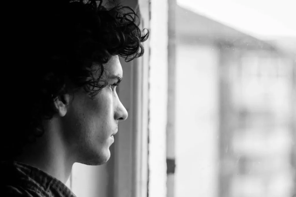 black and white photo of a distraught man looking out a window having a faith crisis