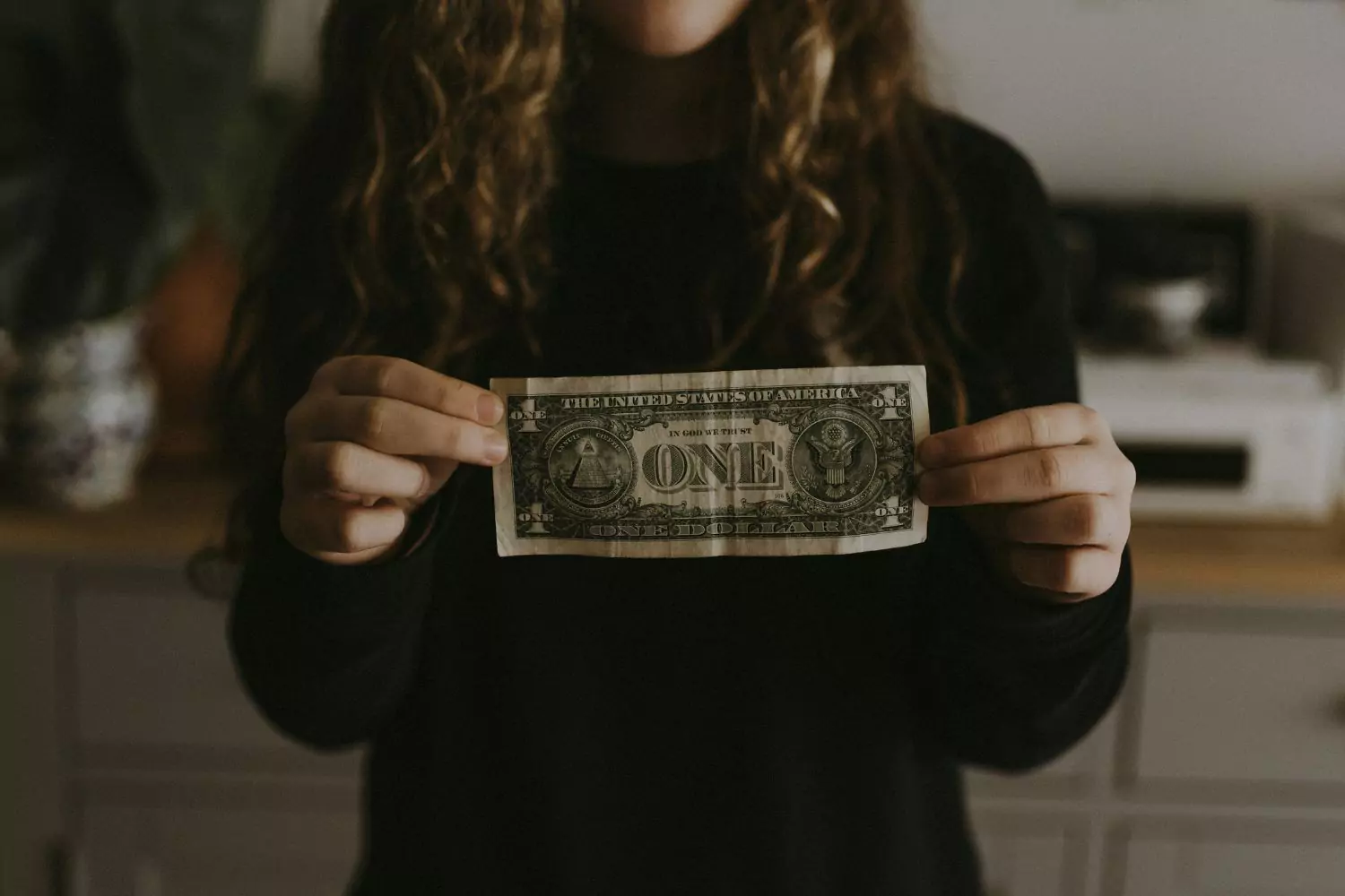 woman holding a US dollar bill, experiencing financial hardship