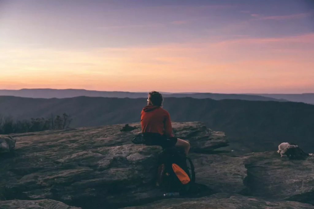 a man resting, sitting on a rock at sunset
