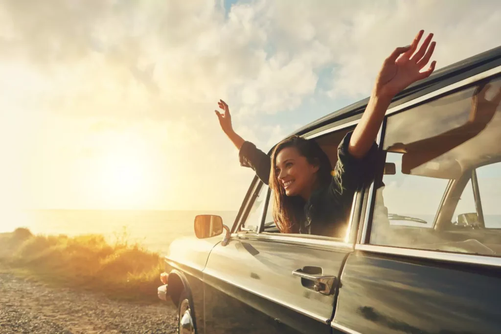 woman leaning out of a car window with her hands in the air living a full life