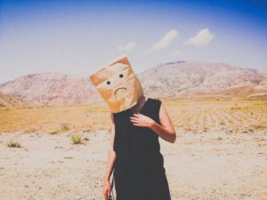a woman with a paper bag over her head stands alone in the desert