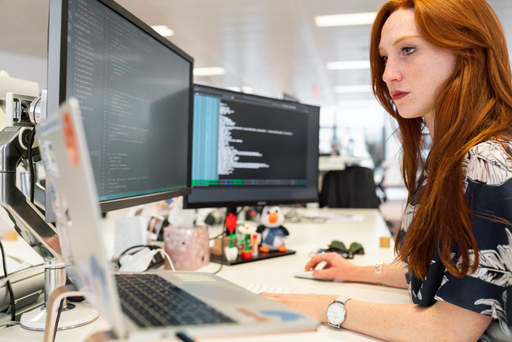 A red-haired woman working on computer coding.