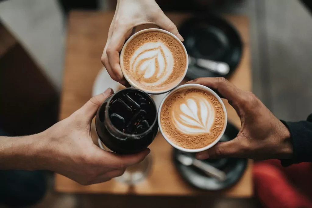 three people holding coffee cups clinking them together