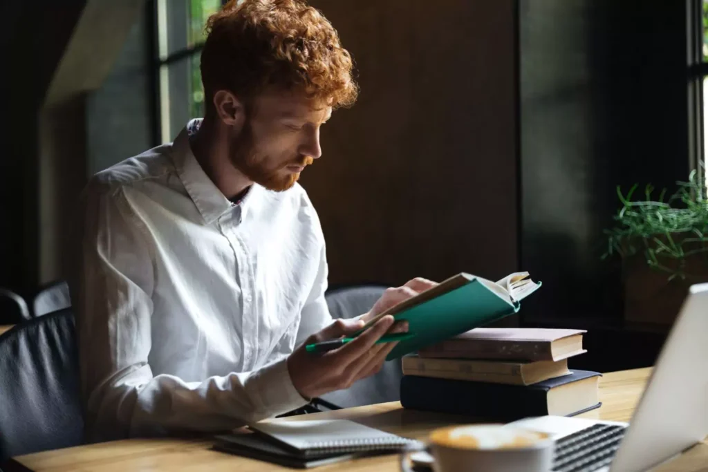 a man reading a book with a stack of books next to him