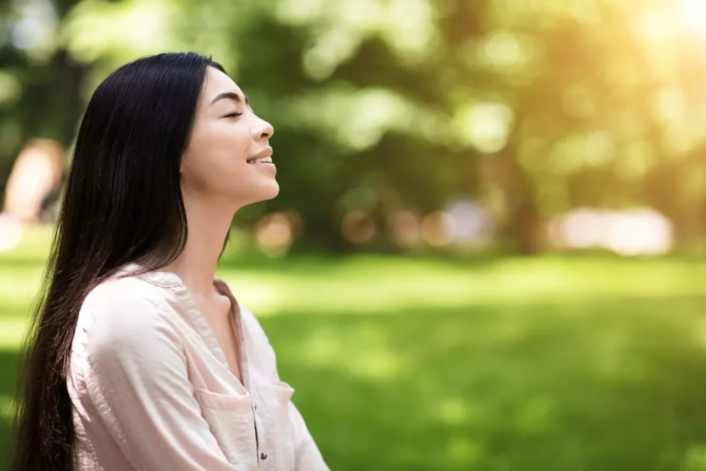 a woman sitting on a park bench with her eyes closed - contentment