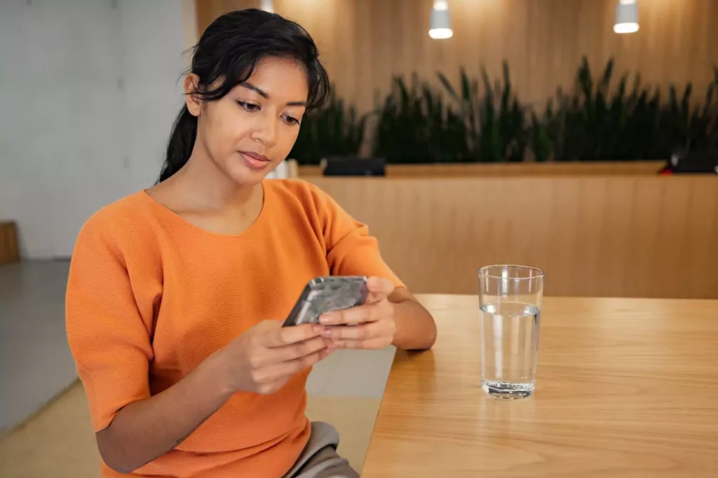 Woman sitting at a table looking at her phone desiring digital minimalism
