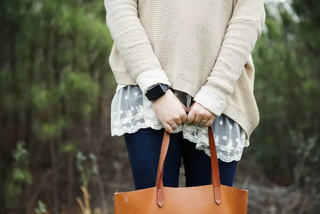 a woman in a cream sweater holding her purse, thinking about purity