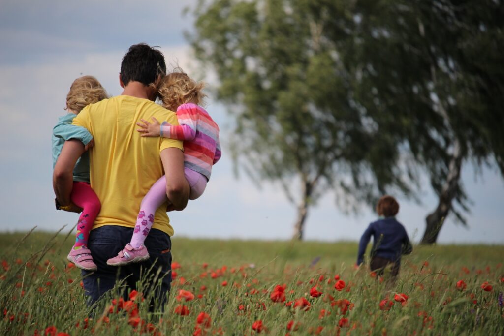 Dad walking in grass carrying two young toddlers.