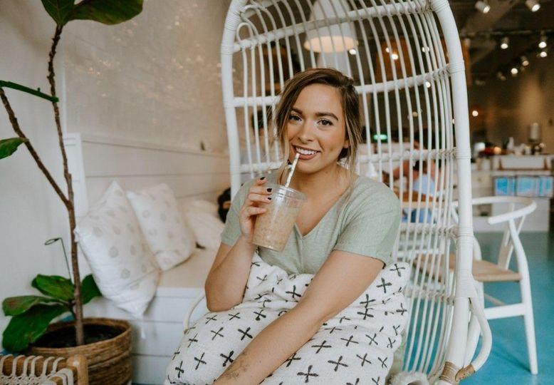 Nastasia sitting on a chair sipping an iced coffee.