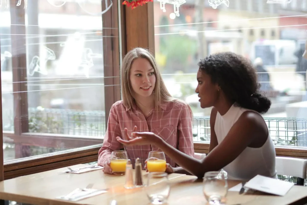two friends drinking orange juice at a cafe, one is meddling in the other's love life
