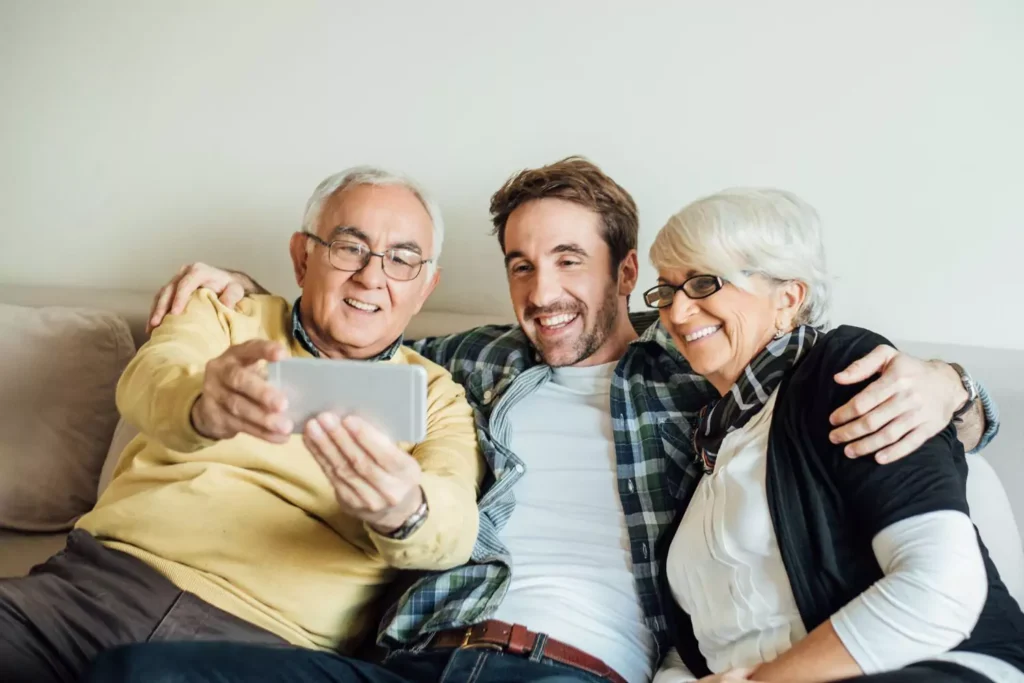 a man sitting with his parents on a couch, taking a selfie. Living with your parents: how to make it work.