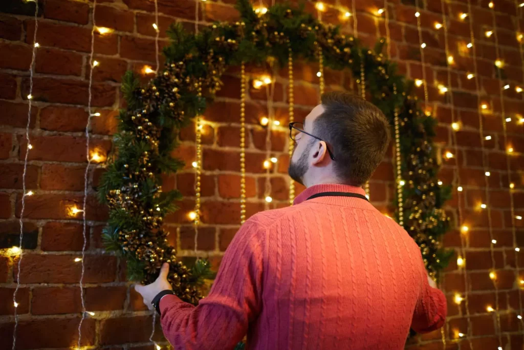 Man hanging up Christmas lights and a wreath with boldness