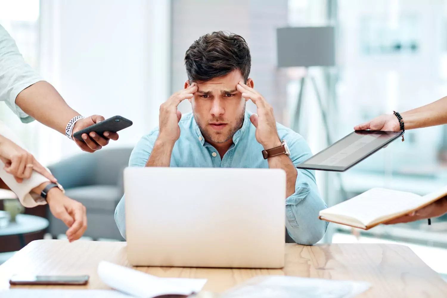 a man sitting at his computer with his hands on his temples. Several hands holding other devices/notes out to him. It's a heavy world