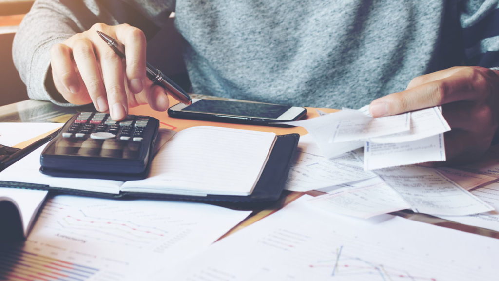 person working on calculator with papers all over table