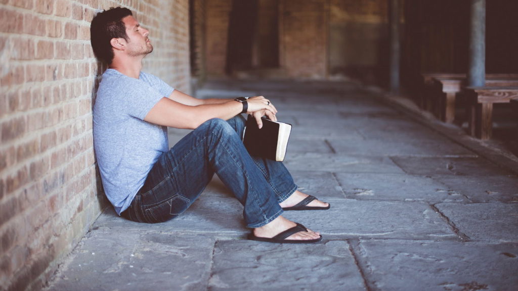 man sitting against wall with Bible