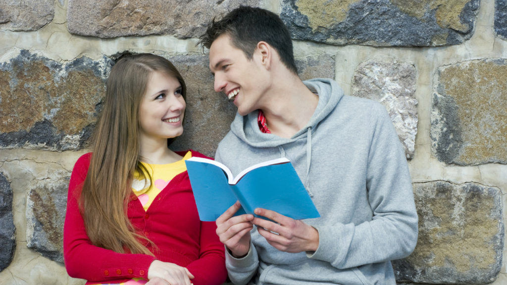 couple leaning against wall smiling at each other