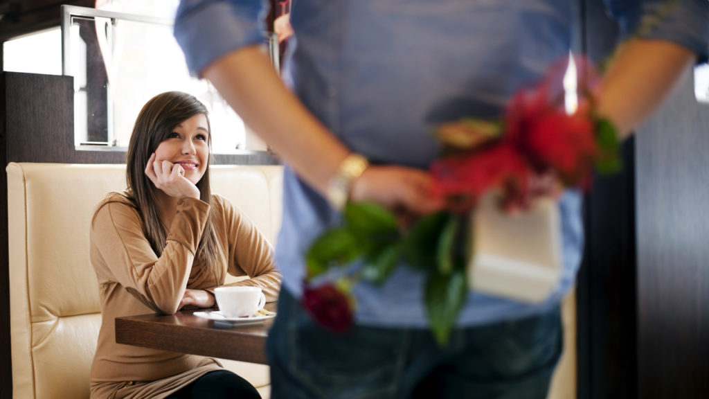 man walking up to woman with flowers behind his back