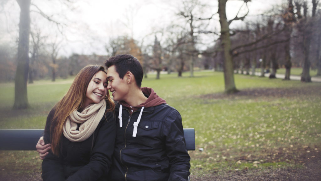 Couple sitting on bench side-hugging in autumn