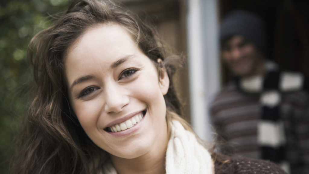 woman smiling at camera with man in the background